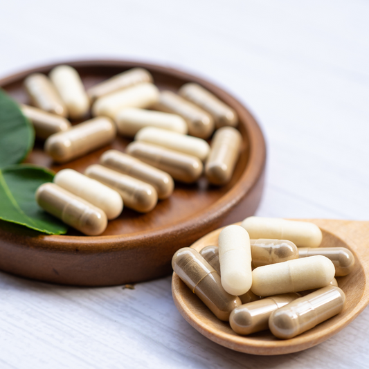 Wooden plates with capsules contining sea moss powder and green leaves on a light background