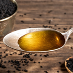 Black seed oil drizzled on a metal spoon, extracted from Nigella sativa seeds, renowned for its antioxidant, anti-inflammatory, and immune-boosting benefits.