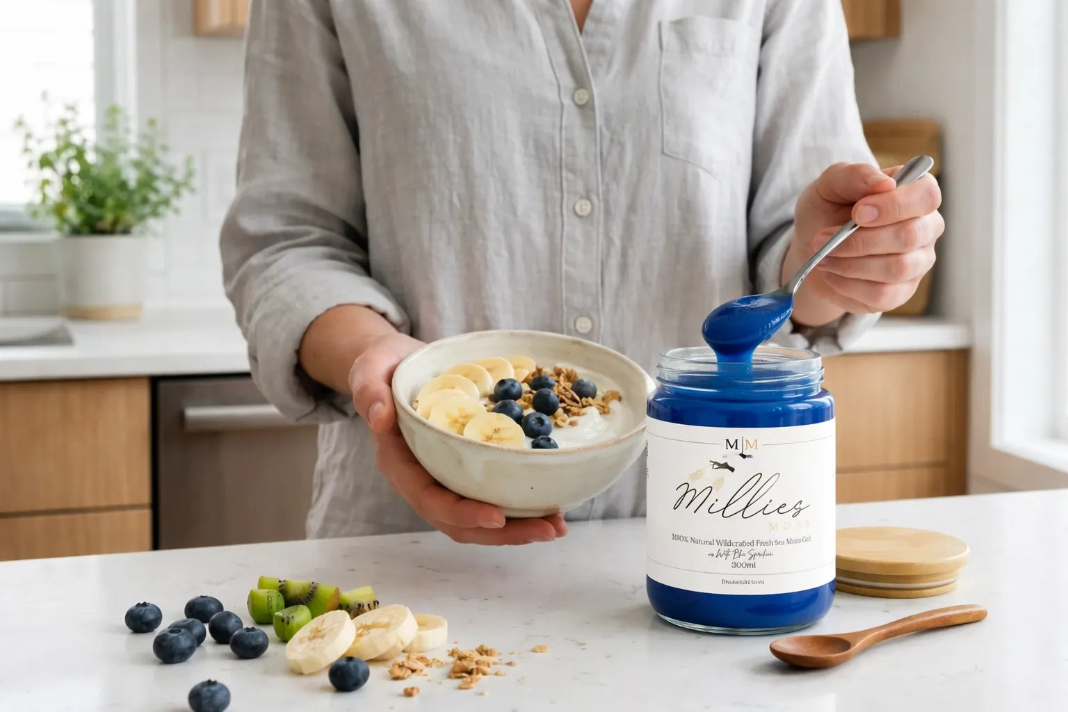 Person adding blue sea moss gel to a breakfast bowl with banana, blueberries and granola