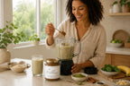 Woman adding Millie’s Moss Cocoa, Matcha and Cinnamon sea moss gel to a smoothie blender in a bright kitchen.