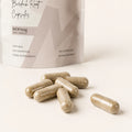 Close-up of Millie’s Moss Burdock Root Capsules with beige plant-based capsules in front of the product pouch