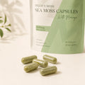 Close-up of Millie’s Moss Sea Moss with Moringa Capsules showing green capsules in front of the product pouch.