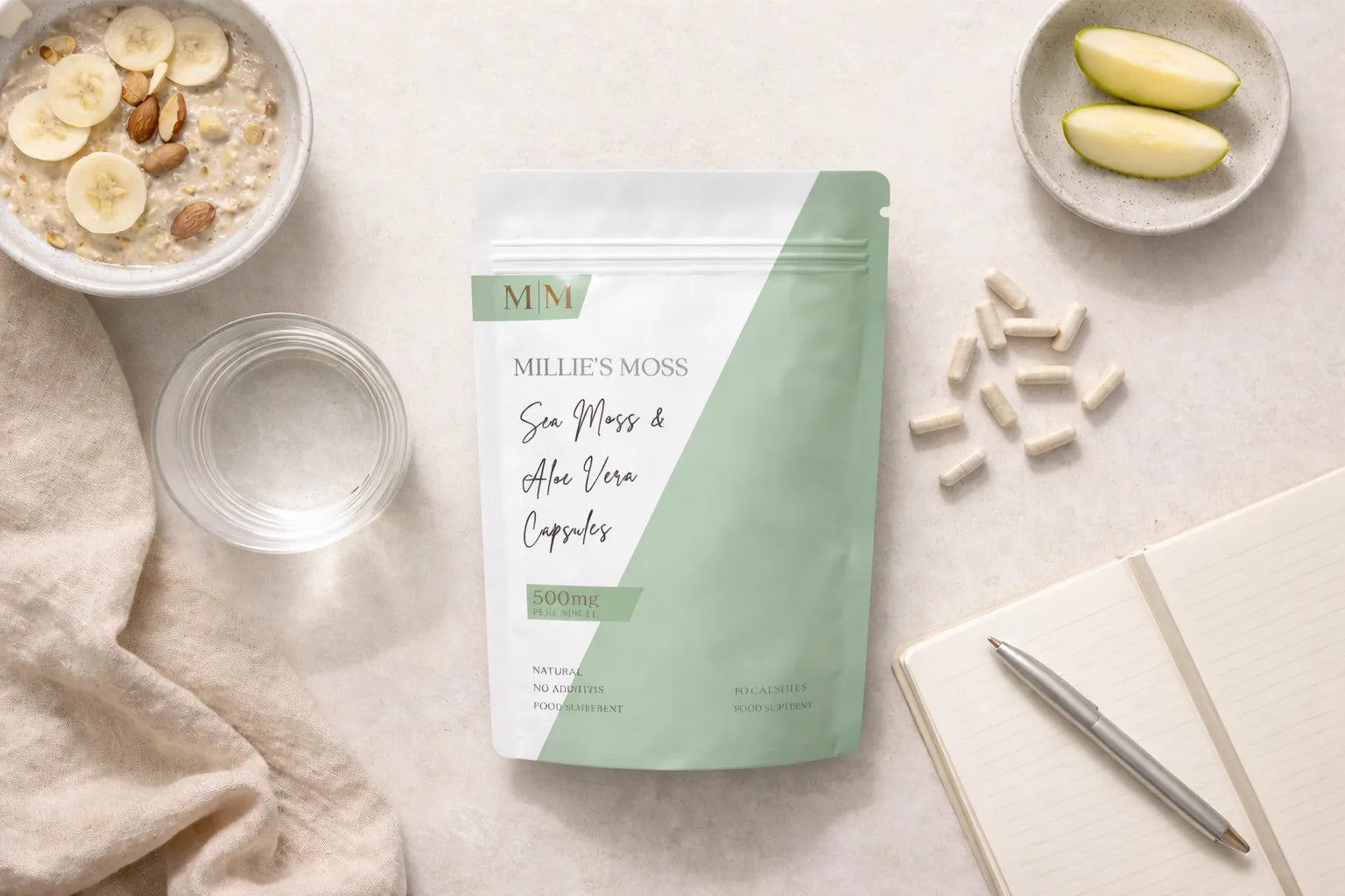 Flat lay of sea moss and aloe vera capsules with breakfast bowl, apple slices, and notebook for a daily wellness routine.