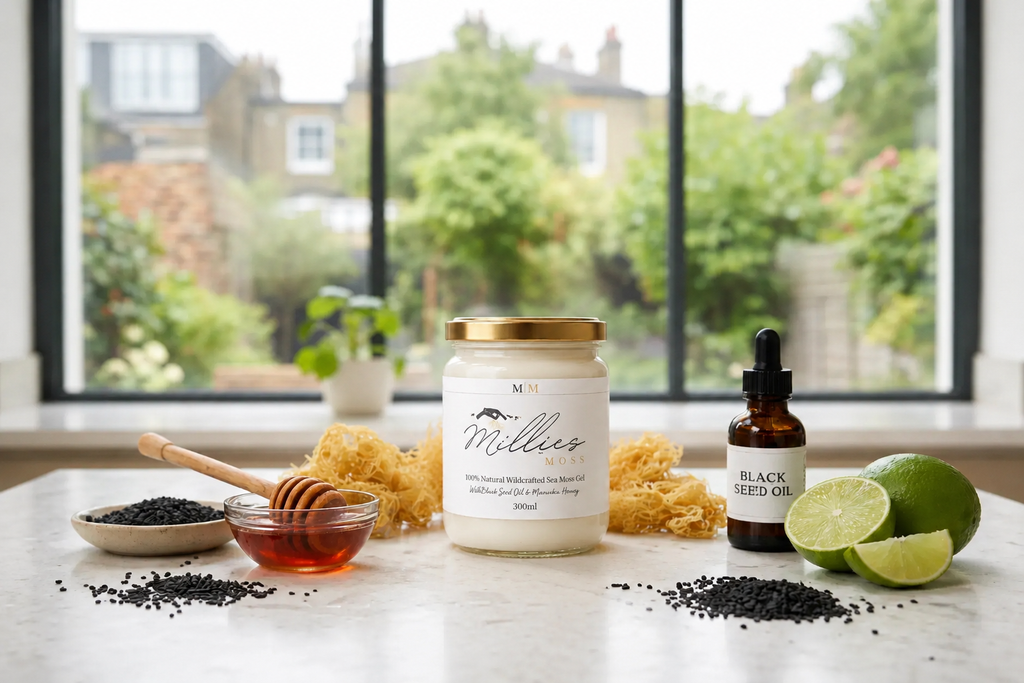 Millie’s Moss sea moss gel jar with black seed oil, honey, lime, raw sea moss and black seeds on a kitchen counter.