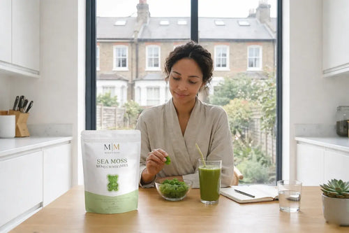 Woman enjoying sea moss gummies supplement at kitchen table with smoothie and healthy morning routine